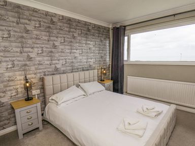 A bedroom with a double bed white bedding bedside tables with lamps and a large window at 315 Filey Road Scarborough