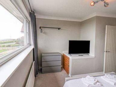 A bedroom corner with a dresser a wall-mounted TV and a window with curtains at 315 Filey Road Scarborough