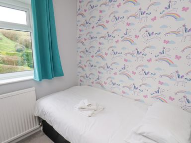 A small bedroom with a bed covered in white linens and towels by a window with turquoise curtains and unicorn wallpaper at 315 Filey Road Scarborough