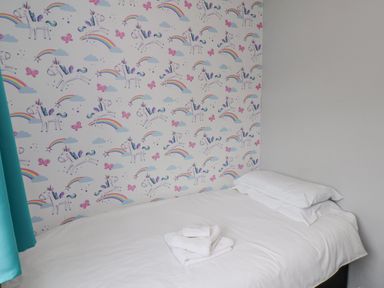 A bed with white linens next to a wall with unicorn and rainbow wallpaper at 315 Filey Road Scarborough