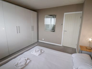 A bedroom with a bed, white wardrobes, a wall mirror, a door, and a bedside table with a lamp at 315 Filey Road in Scarborough