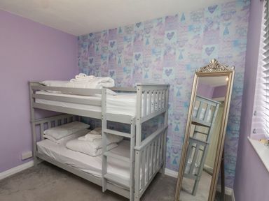 A bedroom with a gray bunk bed with white bedding and a standing mirror against a wall with patterned wallpaper at 315 Filey Road Scarborough