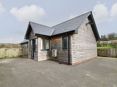 A small wooden cabin with slate roof and fenced yard at Caban Dulas in Rhayader