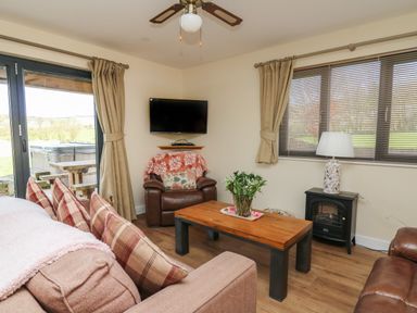 A living room with a sofa and armchairs a wooden coffee table a TV mounted on the wall and a window with blinds at Caban Dulas in Rhayader