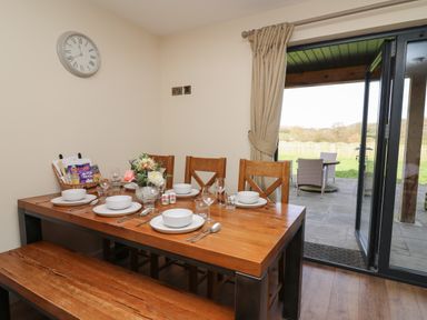 A dining area with a wooden table and chairs set for six people next to a glass door leading to a patio at Caban Dulas in Rhayader