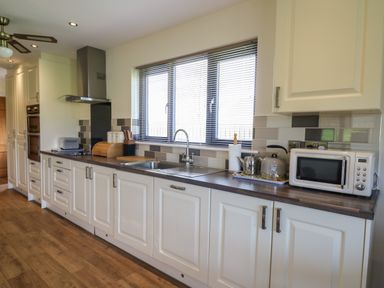 A kitchen with white cabinets a stainless steel sink a microwave and a toaster at Caban Dulas in Rhayader