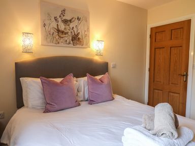 A bedroom with a double bed with two purple pillows towels on the bed and a wooden door at Caban Dulas in Rhayader
