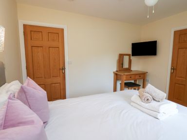 A bedroom with a bed with pink pillows folded towels on the bed a wooden dressing table mounted television and wooden doors at Caban Dulas in Rhayader