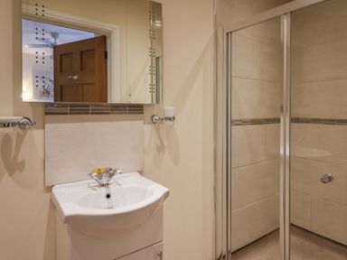 A bathroom with a white sink, a mirror above it, and a shower with glass doors at Caban Dulas in Rhayader