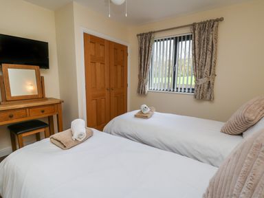 A bedroom with two single beds towels pillows a wooden dresser with a mirror a television window with curtains at Caban Dulas in Rhayader