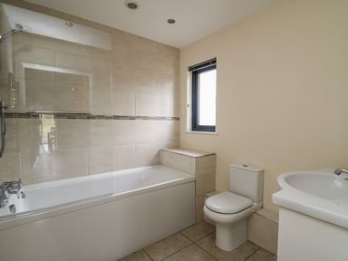A bathroom with a bathtub shower combo, a toilet, a sink, and a window at Caban Dulas in Rhayader