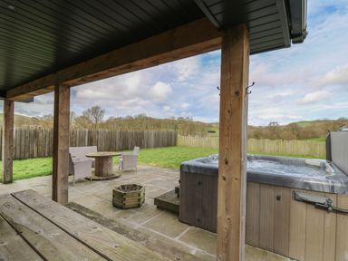 A covered patio with wooden posts and a hot tub next to a patio table and chairs at Caban Dulas in Rhayader