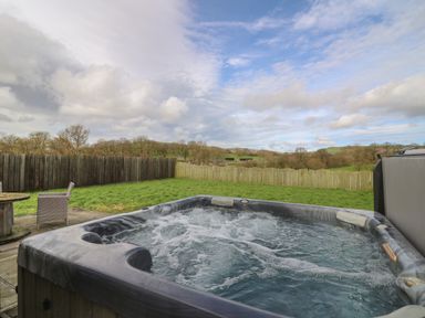 An outdoor hot tub with bubbling water on a patio next to grass and a wooden fence at Caban Dulas in Rhayader