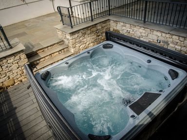 An outdoor hot tub with bubbling water next to stone walls and metal railings at Pen-y-Ghent in Kirkby Lonsdale