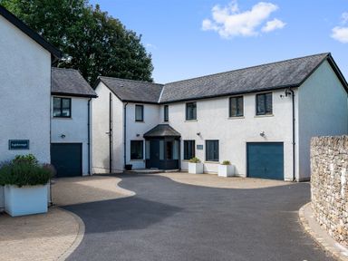 A driveway with white two story buildings and garage doors with plants in pots at Pen-y-Ghent in Kirkby Lonsdale