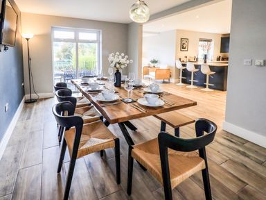 A dining area with a wooden table set with bowls glasses and cutlery black chairs and a view into a kitchen with bar stools at Pen-y-Ghent in Kirkby Lonsdale