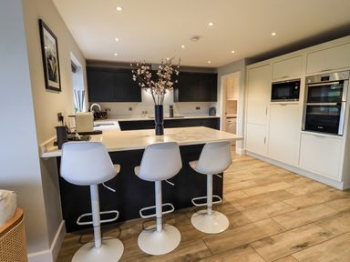 A kitchen with a white island counter and three white bar stools at Pen-y-Ghent in Kirkby Lonsdale