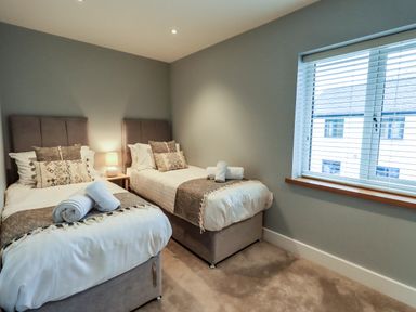 A bedroom with two single beds a bedside table with a lamp and a window with blinds at Pen-y-Ghent in Kirkby Lonsdale