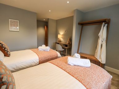 A bedroom with two single beds a desk with a lamp and chair a wall-mounted clothes rack and bathrobes at Pen-y-Ghent in Kirkby Lonsdale