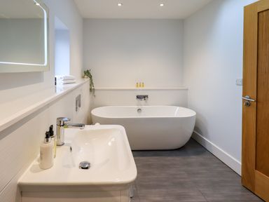 A bathroom with a bathtub sink towels and a wooden door at Pen-y-Ghent in Kirkby Lonsdale
