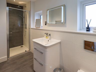 A bathroom with a shower enclosure a sink with two drawers a lighted mirror and a window at Pen-y-Ghent in Kirkby Lonsdale