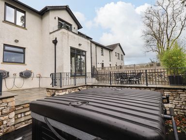 An outdoor patio area with a black hot tub and metal railing next to a white building at Pen-y-Ghent in Kirkby Lonsdale