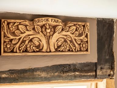 A carved wooden sign with leaves and flowers and the words Brook Farm above a doorway at Brook Farm in St Nicholas near Halesworth