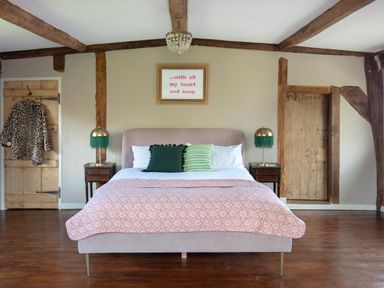 A bedroom with a bed two bedside tables and lamps exposed wooden beams and two wooden doors at Brook Farm in St Nicholas near Halesworth