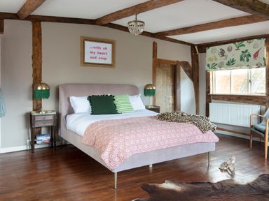 A bedroom with a bed pink patterned bedspread green pillows wooden beams and a window with floral blind at Brook Farm St Nicholas near Halesworth
