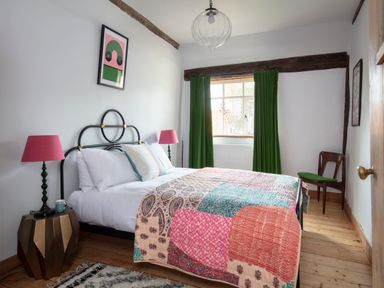 A bedroom with a double bed with patterned quilt green curtains and two pink lamps at Brook Farm in St Nicholas near Halesworth