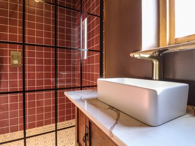 A bathroom with a white rectangular sink on a marble countertop and a shower with red tiled walls and a black grid door at Brook Farm in St Nicholas near Halesworth