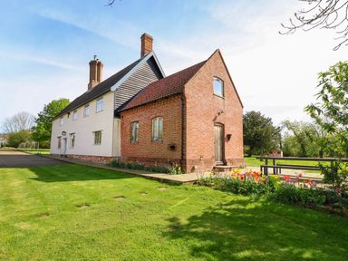 A brick and white house with a red tiled roof surrounded by grass and flowers at Brook Farm in St Nicholas near Halesworth