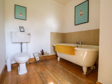 A bathroom with a white toilet and a freestanding bathtub with a yellow towel on wooden floor at Brook Farm in St Nicholas near Halesworth