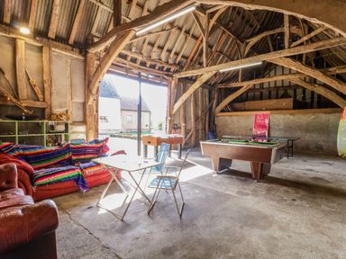 A barn converted into a recreational room with a pool table a foosball table a small table with chairs and a couch with colorful blankets at Brook Farm in St Nicholas near Halesworth