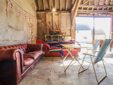 A rustic indoor space with two leather sofas a foldable table and two folding chairs at Brook Farm in St Nicholas near Halesworth