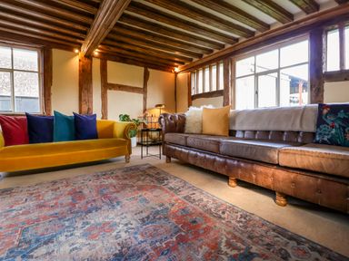 A living room with two sofas a patterned rug wooden beams and large windows at Brook Farm in St Nicholas near Halesworth