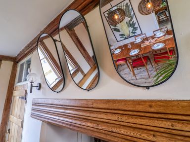 Three oval mirrors on a wall reflecting a dining table with chairs and table setting at Brook Farm in St Nicholas near Halesworth