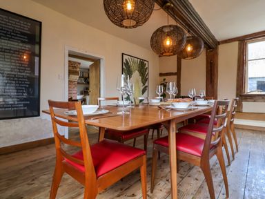 A dining room with a wooden table set for eight with red cushioned chairs and hanging wicker light fixtures at Brook Farm in St Nicholas near Halesworth