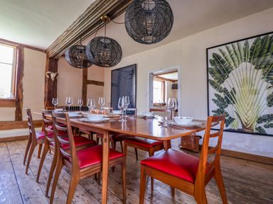 A dining room with a wooden table and red cushioned chairs set with bowls and glasses at Brook Farm in St Nicholas near Halesworth