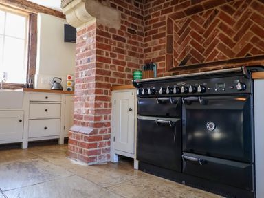 A kitchen with a black stove oven a brick chimney and white cabinets at Brook Farm in St Nicholas near Halesworth
