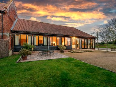 A building with tiled roof and large windows next to a patio with table and chairs and a grassy lawn at Mallard in Wheatacre