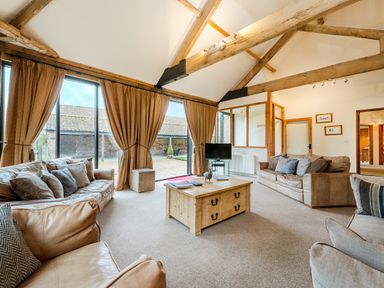 A sitting room with leather sofas a wooden coffee table and large windows with curtains at Mallard in Wheatacre
