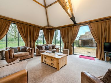 A sitting room with leather sofas wooden coffee table and large windows with curtains at Mallard in Wheatacre