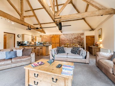 An open living room with exposed wooden beams a sofa wooden coffee table kitchen area and dining table at Mallard in Wheatacre