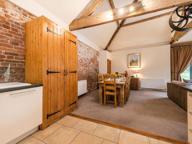 A dining area with wooden table and chairs next to a wooden cabinet and exposed brick wall at Mallard in Wheatacre