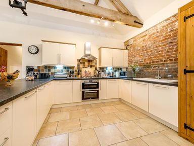 A kitchen with white cabinets black countertops a tiled backsplash exposed wooden beams and a brick wall at Mallard in Wheatacre