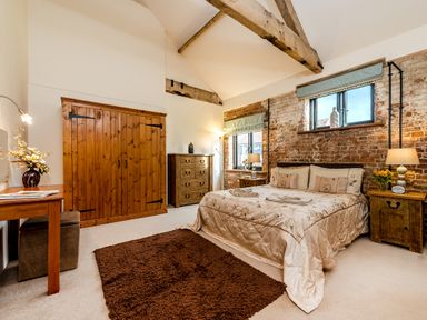 A bedroom with a double bed bedside tables wooden dresser wardrobe and exposed brick wall at Mallard in Wheatacre