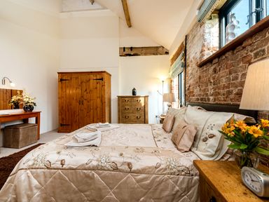 A bedroom with a bed a wooden wardrobe a chest of drawers and flowers on a bedside table at Mallard in Wheatacre