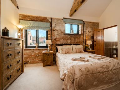 A bedroom with a bed two bedside tables a chest of drawers and brick walls at Mallard in Wheatacre