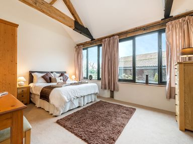 A bedroom with a bed nightstands wooden furniture and large windows at Mallard in Wheatacre